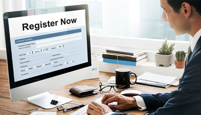 Man using a computer to fill out a registration form with "Register Now" displayed on the screen, relevant to NDIS compliance services by Compliance Care.