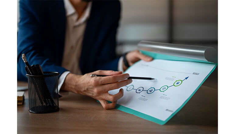 Person pointing at a risk assessment chart on paper, illustrating compliance steps for NDIS services, with a pen in hand and a pen holder nearby.