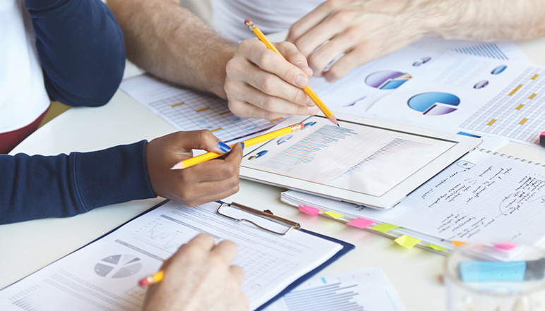 Hands collaborating over documents and a tablet displaying graphs, emphasizing teamwork in audit preparation and compliance related to NDIS certification.